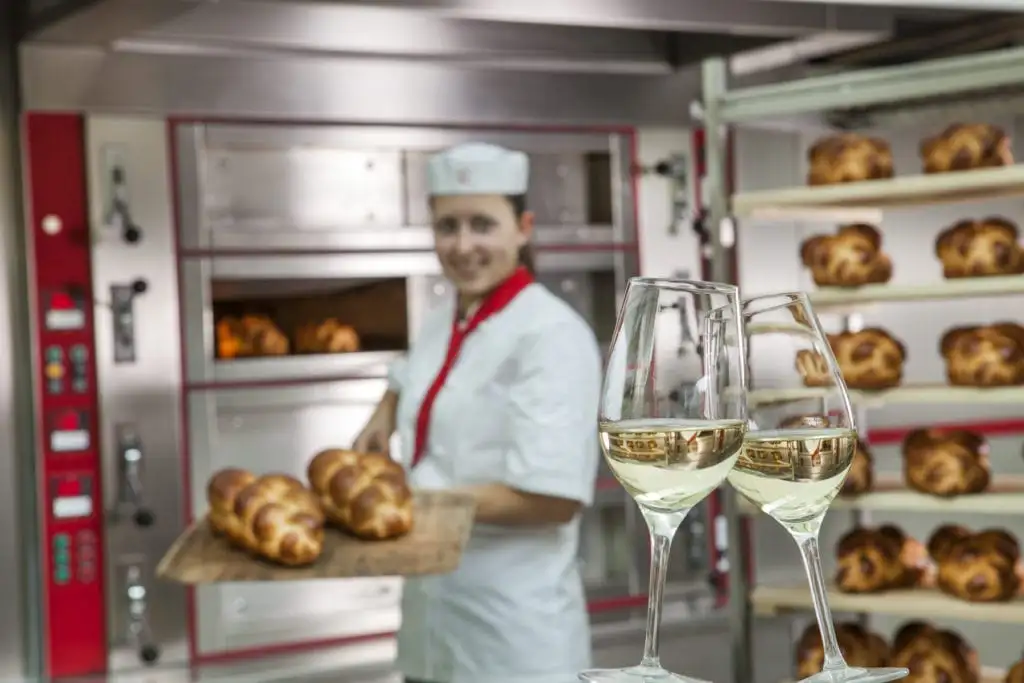 Eine Köchin hält zwei Weingläser vor einer Bäckerei.